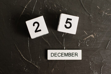 Flatlay wooden calendar with the date December 25 on a dark textured background.