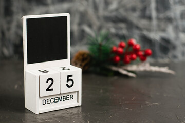 Wooden calendar with December 25 date and beautiful Christmas decoration on dark textured background with copy space
