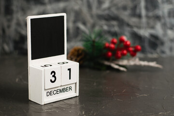 Wooden calendar with December 31 date and beautiful Christmas decoration on dark textured background with copy space