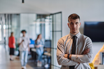 A young business leader stands with crossed arms in a modern office hallway, radiating confidence and a sense of purpose, embodying a dynamic and inspirational presence.