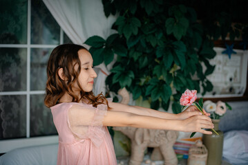 A little girl in a pink dress holds a pink flower in her hands and enjoys its beauty