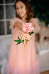 A little girl in a pink dress holds a pink flower in her hands and enjoys its beauty