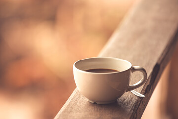 A white cup of coffee on wooden with morning light background texture