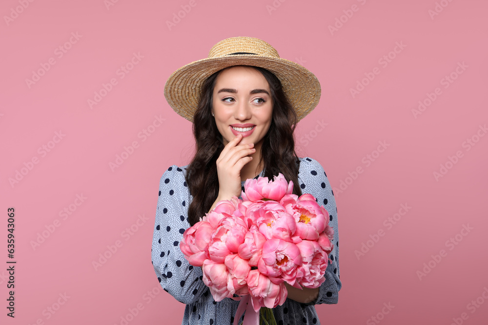 Wall mural Beautiful young woman in straw hat with bouquet of peonies on pink background