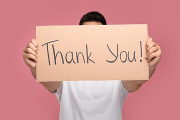 Man holding cardboard sheet with phrase Thank You on pink background, selective focus