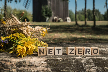 Drewniane klocki z napisem  NET ZERO na tle bukietu z kwiatów polnych oraz łąki z wiatrakiem w słoneczny dzień. - obrazy, fototapety, plakaty