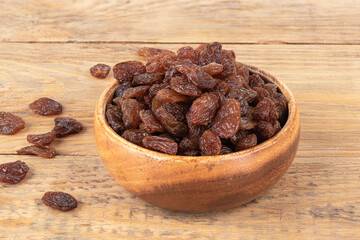 Sweet dehydrated raisins in a bowl and on a wooden background.