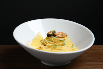 Tasty capellini with mussels and lemon on wooden table, closeup. Exquisite presentation of pasta dish