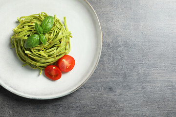Tasty tagliatelle with spinach and tomatoes served on grey table, top view and space for text. Exquisite presentation of pasta dish