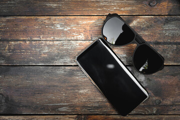 Fashionable male sunglasses and mobile phone on the old wooden table close up background with copy space. Top view.