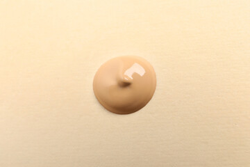 Drop of skin foundation on beige background, top view