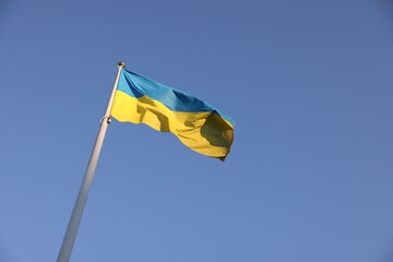 Flag of Ukraine fluttering against blue sky, low angle view. Space for text
