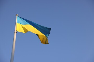Flag of Ukraine fluttering against blue sky, low angle view. Space for text