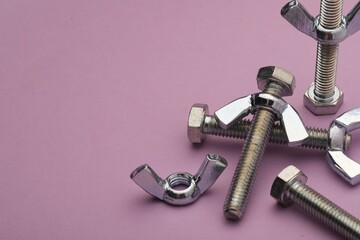 Metal screws with wing nuts on purple background, closeup. Space for text