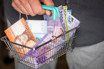 Chile Money in Shopping Cart. A man holding a basket with Chilean pesos currency in his hand,...