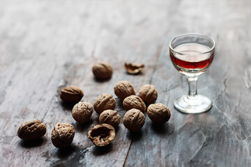 A glass of walnut liquor and walnuts on the old wooden table in backlight