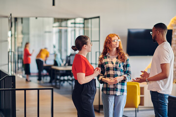 Group of business colleagues, including an African American businessman, engage in a conversation about business issues in the hallway of a modern startup coworking center, exemplifying dynamic