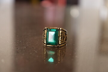 An Ancient Golden Ring embedded with Green Emerald Stone Gem on a shiny brown marble 
