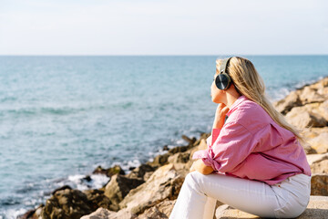 Woman sitting near waving seashore and listening to music