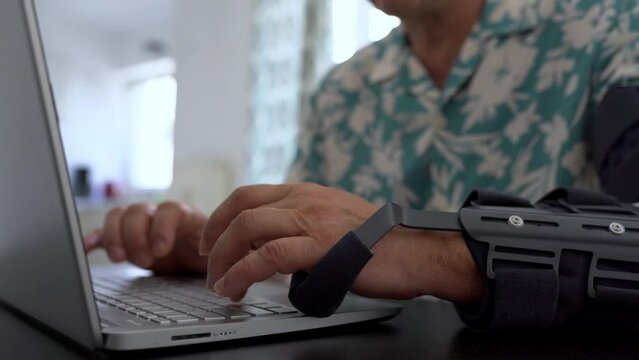 Man with adjustable articulated elbow orthosis typing on laptop keyboard