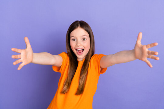 Portrait of young funky schoolgirl wear orange t shirt friendly welcome you hello world meeting people isolated on violet color background