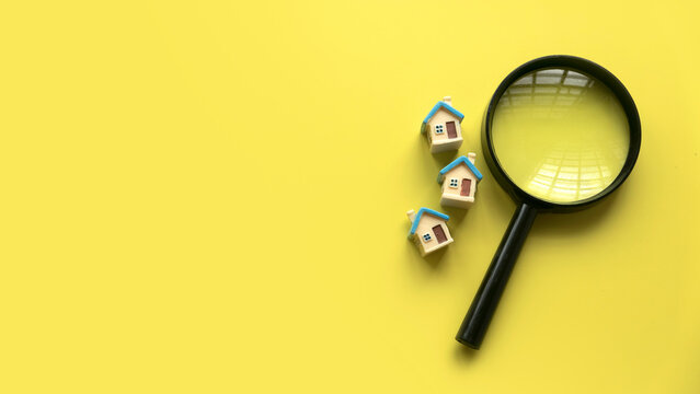 House searching concept. House inspection. Miniature house with magnifying glass over a yellow background with copy space.