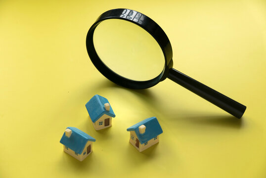 House searching concept. House inspection. Miniature house with magnifying glass over a yellow background.