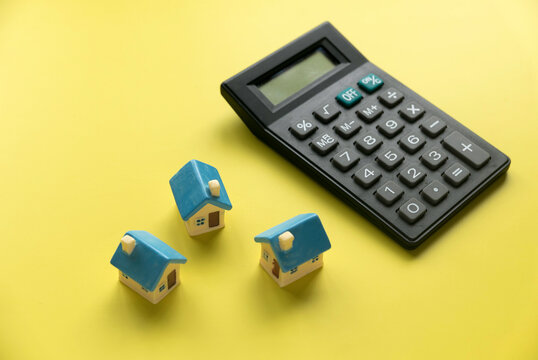 Concept of home loan mortgage, refinance, interest rate. Saving for house.Miniature house with calculator over yellow background.