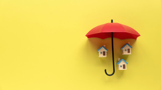 Concept of renters home insurance or mortgage protection. House under a red umbrella on yellow background with copy space.