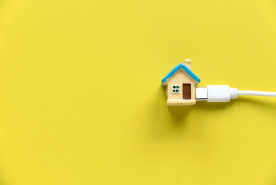 House and utilities concept. Miniature house attach to a white cable over a yellow backgorund
