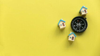 Miniature house and a compass over a yellow background with copy space.