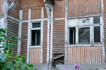 Facade of an old wooden cottage with open windows and rotten boards