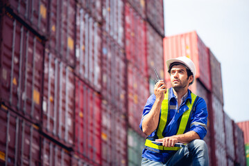 Engineers or industrial workers using walkie-talkie command or communicate to shipping cargo freights colleague with background of cargo containers at shipping container yards and port yards.
