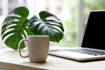 Coffee cup and monstera plant leaf with laptop on table.