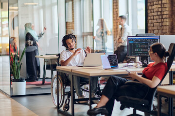 Fototapeta na wymiar A young business group, including an African American businessman in a wheelchair, collaborates within a modern glass office, actively engaged around a computer and laptop, collectively solving