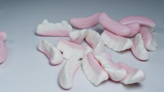 Gummy candies in the shape of jaws with different teeth fall onto a white table.