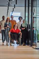 Fototapeta premium A diverse group of young business people walking a corridor in the glass-enclosed office of a modern startup, including a person in a wheelchair and a woman wearing a hijab, showing a dynamic mix of