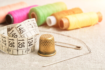 Sewing kit of needle, thimble, thread and measuring meter.On gray concrete table top.