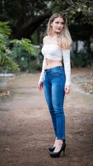 Obraz premium Blonde girl in a white top and blue jeans posing outdoors
