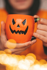Portrait of candid authentic zoomer boy posing with jack lantern mug and sweets at halloween party