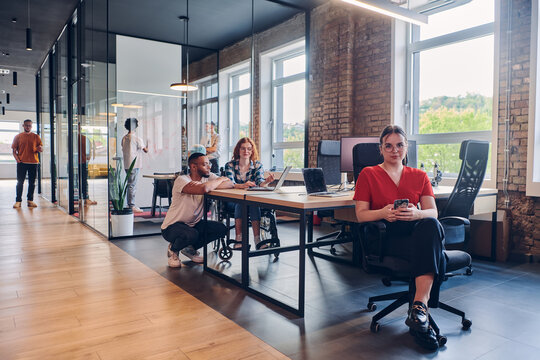 A diverse group of business professionals collaborates in a modern startup coworking center, utilizing a mix of paper-based and technological tools such as mobile phones and computers to collectively