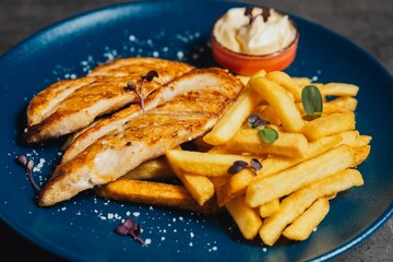 Closeup of a plate of french fries with a chicken breast steak and sauce