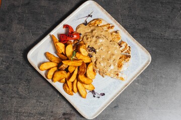 Closeup of a plate of french fries with a chicken breast steak and sauce