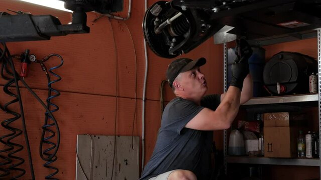 A car mechanic unscrews the crankcase protection in a modern car.