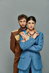 portrait of man in glasses and woman looking at camera, models in trendy suits, grey background