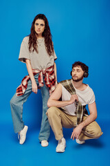 Obraz na płótnie Canvas trendy couple, college students in casual attire, headphones, music, bold makeup, blue backdrop