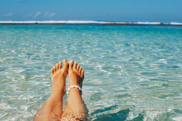 Beautiful women's legs with a white bracelet made of shells against the background of the ocean. A stylish concept for leisure and travel with space for text