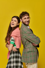 happy stylish man and woman standing back to back, posing, yellow background, student outfit, laugh