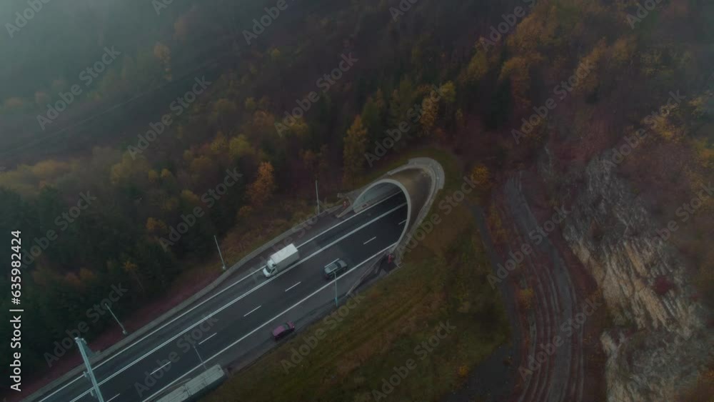 Poster drone view above cars driving in a tunnel between fields and trees during foggy weather