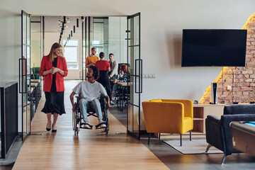 A group of young business people in a modern glass-walled office captures the essence of diversity and collaboration, while two colleagues, including an African American businessman in a wheelchair